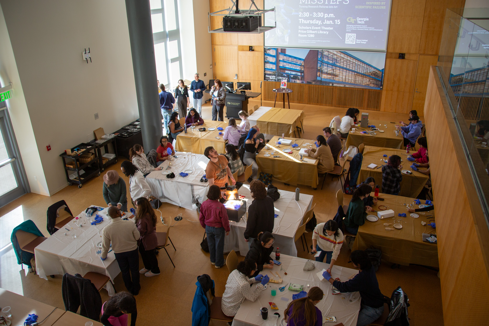 Overhead view of the Georgia Tech Library during the “Cosmic Missteps: Turning Research Failure Into Art” event, featuring many tables filled with attendees engaged in collaborative art-making throughout the open atrium.